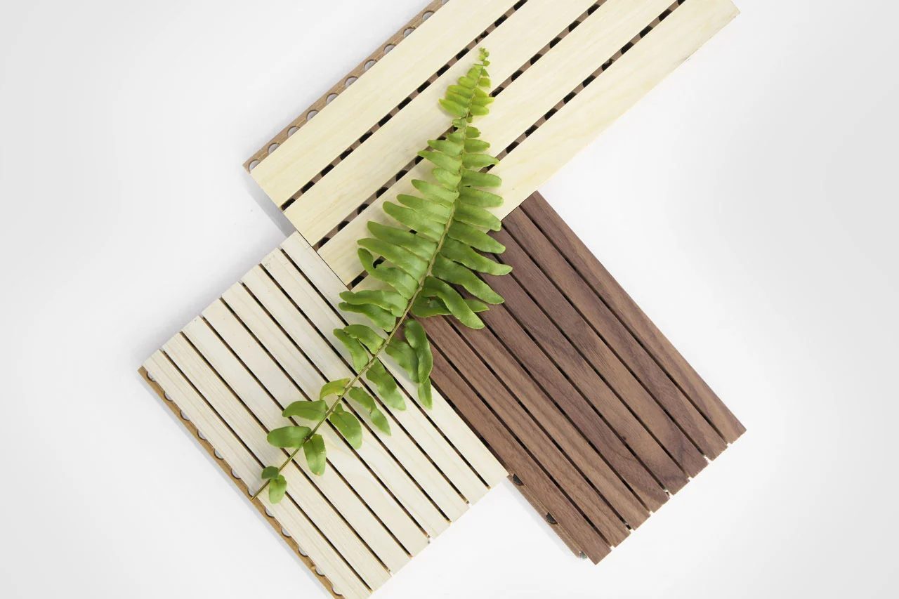 A collection of grooved wooden panels in light and dark shades, with a green fern leaf placed on top, representing eco-friendly design.