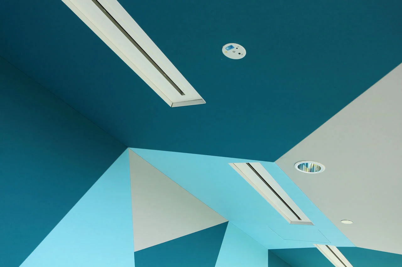 A ceiling features geometric patterns in various shades of blue with two rectangular air vents, a round smoke detector, and a recessed ceiling light.