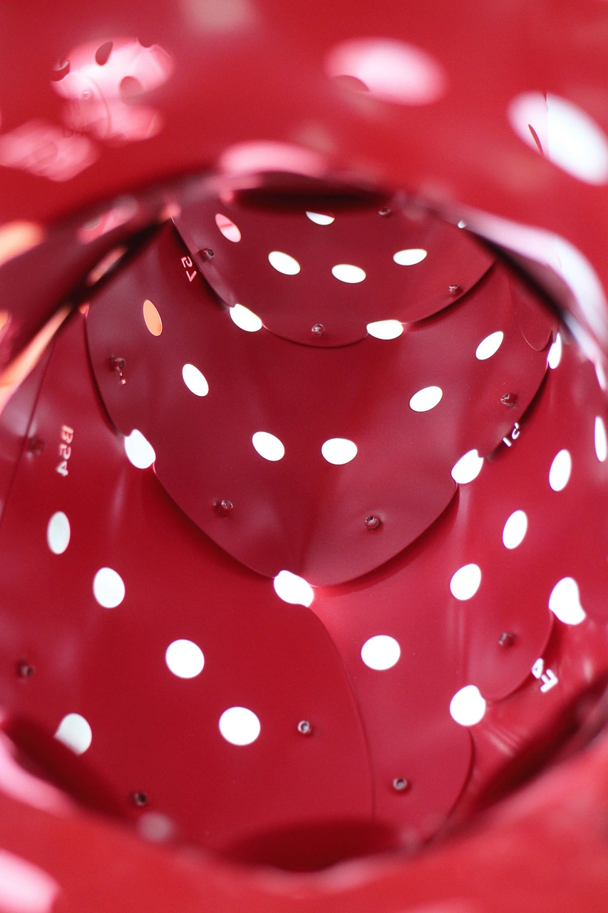 Close-up of a red, perforated structure with white polka dots, creating an abstract, tunnel-like visual effect.