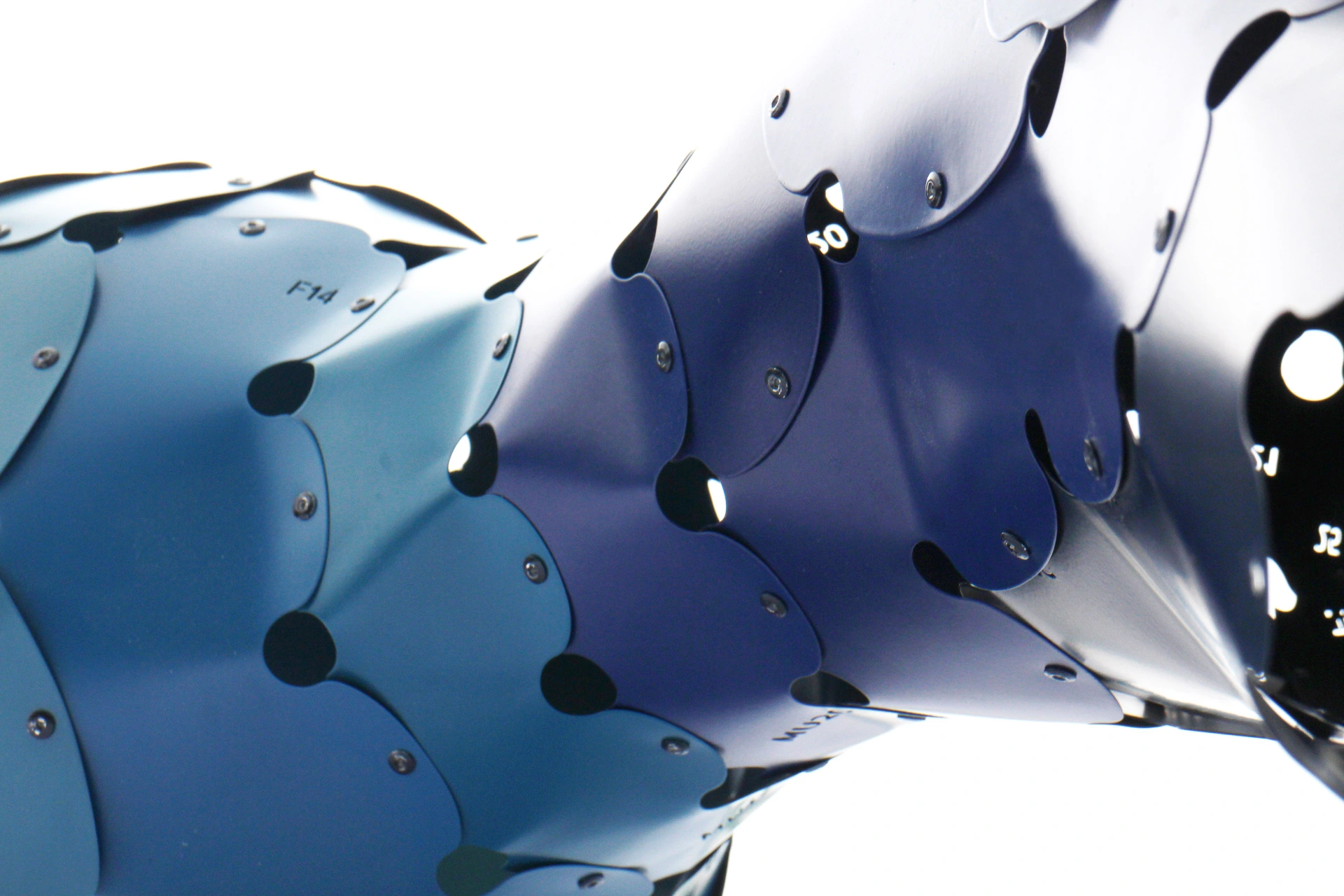 A detailed view of interlocking metal scales in shades of blue, forming a sleek and futuristic design, with visible screws holding the structure together.