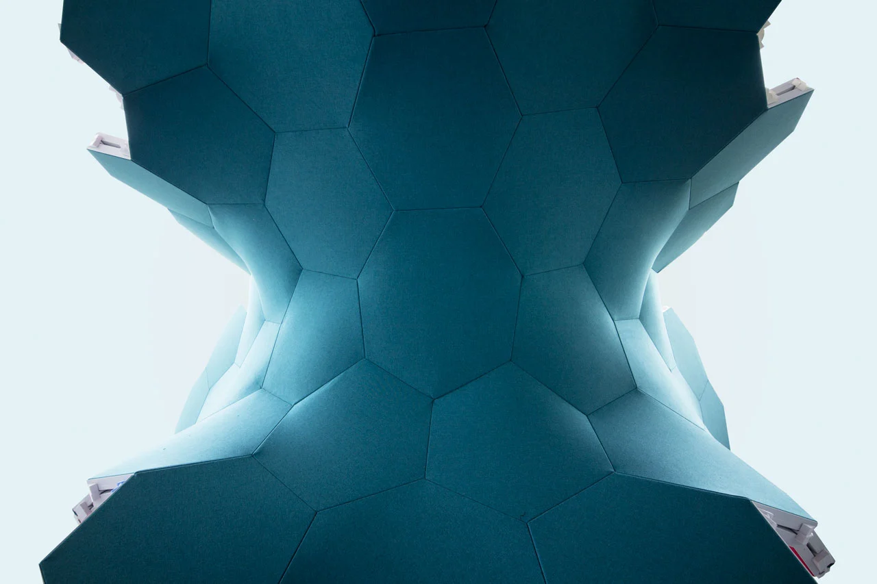 A backlit, hexagonal patterned structure in teal, creating an organic, flowing shape with soft gradients of light between the edges.