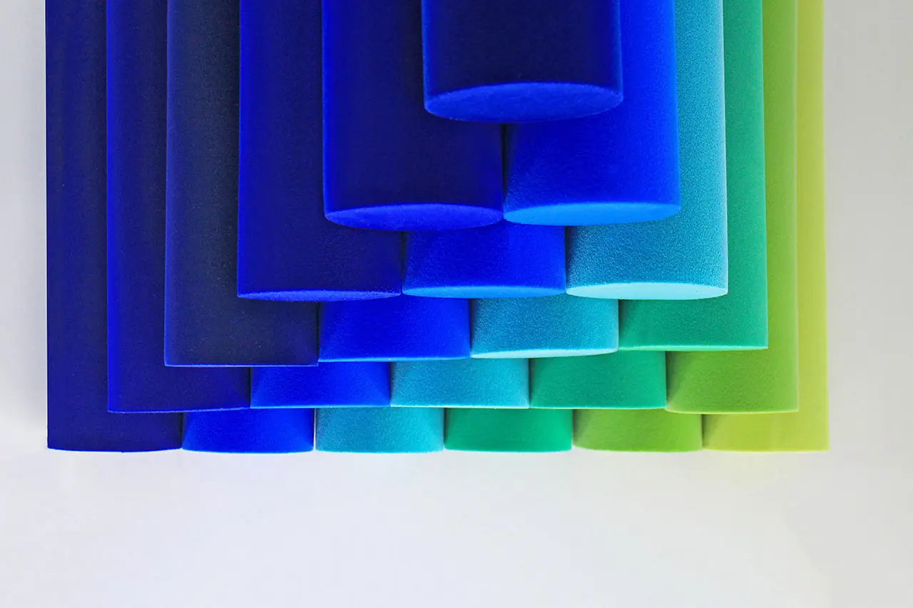 A series of cylindrical blue foam blocks in varying shades of blue and green, stacked in a gradient pattern against a white background.
