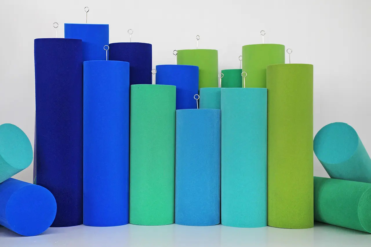 Cylindrical foam rollers in shades of blue and green stand upright in varying heights, with some lying horizontally at the sides. Several have metal hooks on top, all against a plain white background.