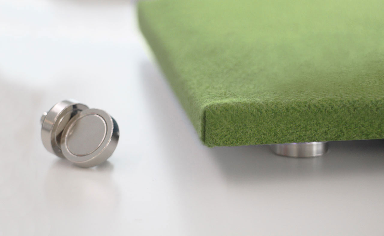 A close-up of a green felt-like square panel supported by a metallic stand, with another round metallic element placed next to it, against a white background.