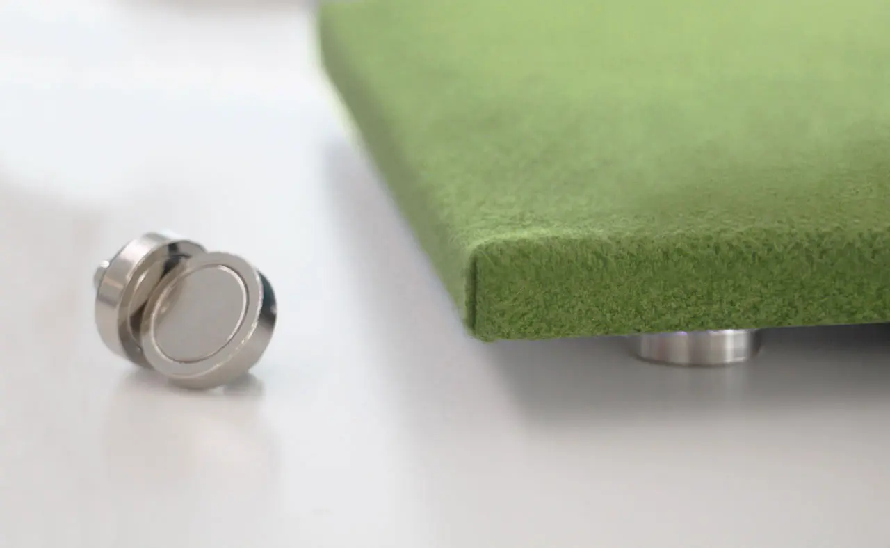A close-up of a green felt-like square panel supported by a metallic stand, with another round metallic element placed next to it, against a white background.