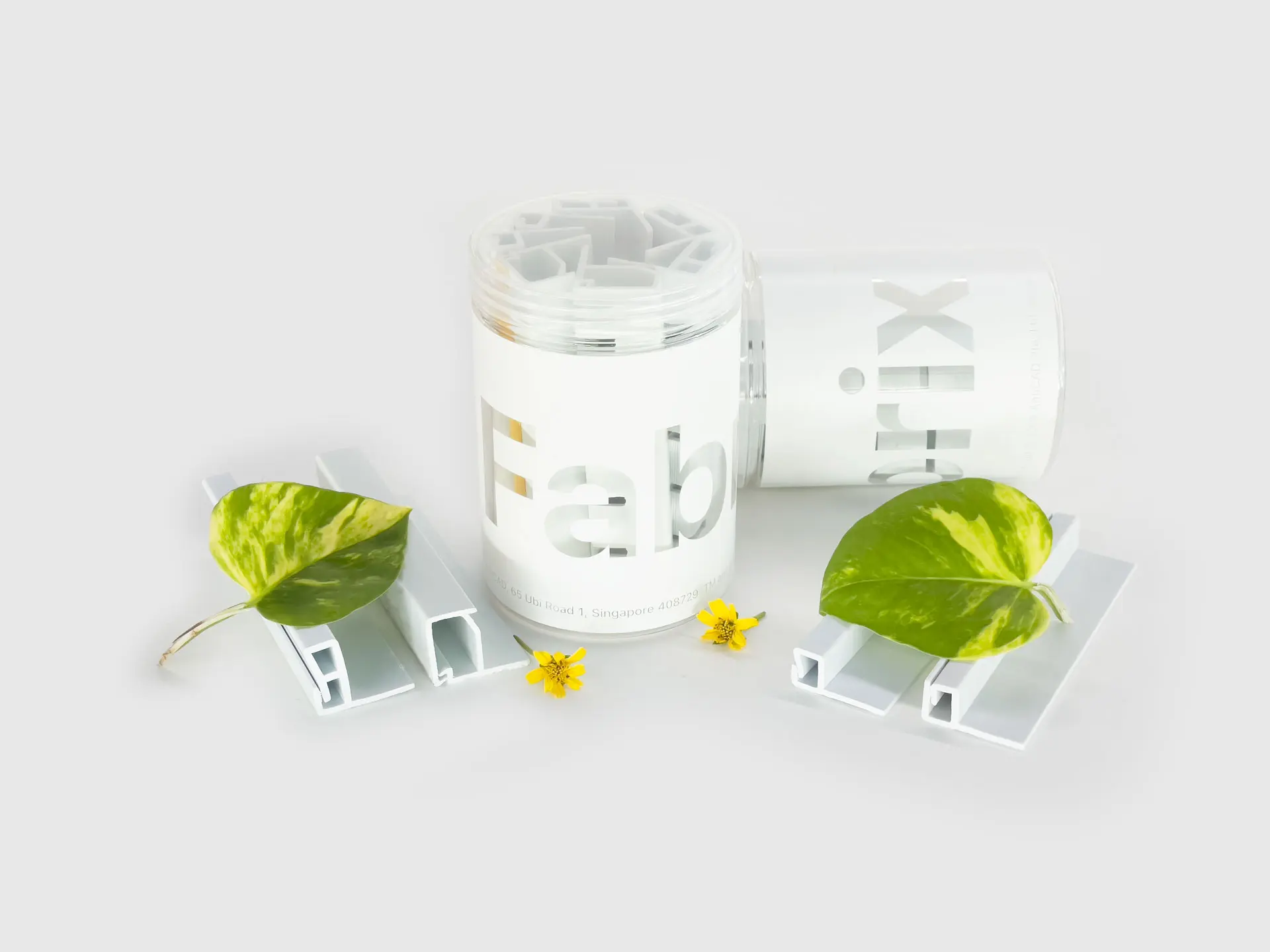 A sleek, minimalist product display featuring white "Fabrix" packaging, complemented by green leaves and a yellow flower, emphasizing eco-friendly design.