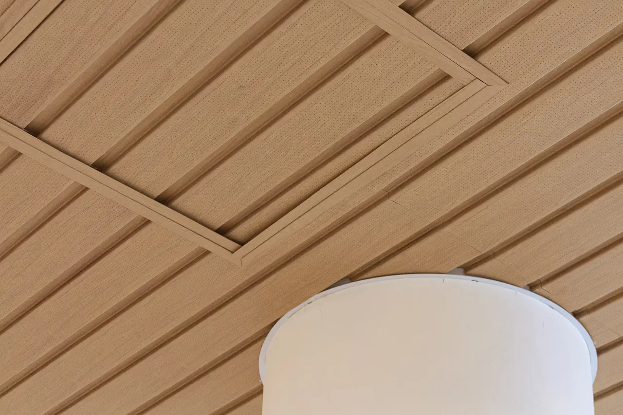 A close-up of a wooden ceiling with rectangular paneling. A white circular structure, possibly a light fixture or column, is integrated into the ceiling.