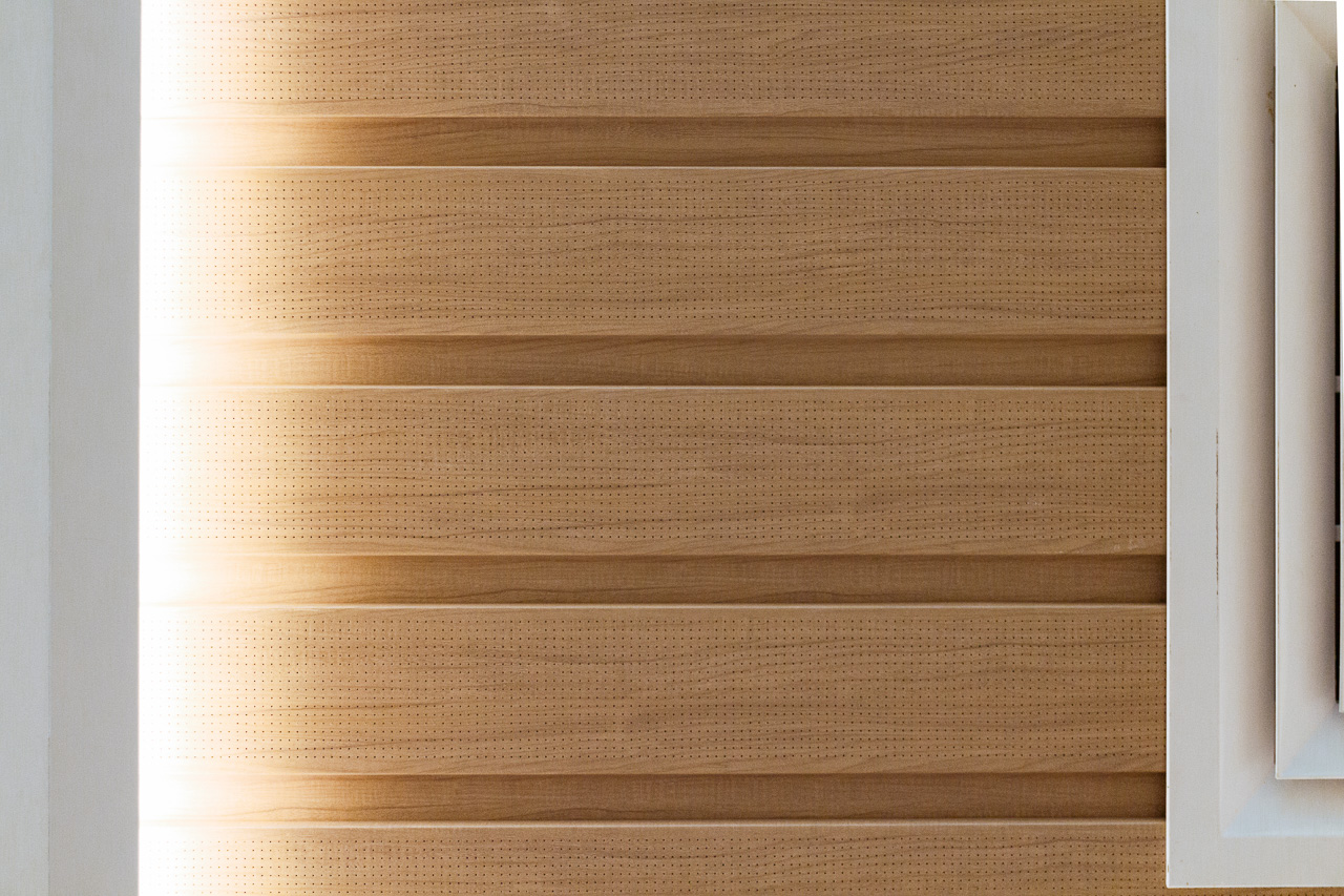 A close-up of light brown wooden wall panels with perforated, horizontal slats, highlighted by sunlight.