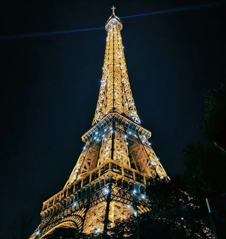 The Eiffel Tower in Paris illuminated with golden lights at night, standing tall against a dark sky.