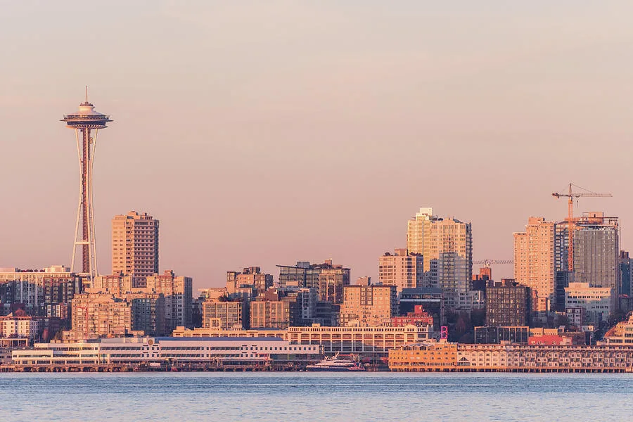 A cityscape of Seattle at sunset featuring the iconic Space Needle, with downtown buildings and waterfront in the foreground.