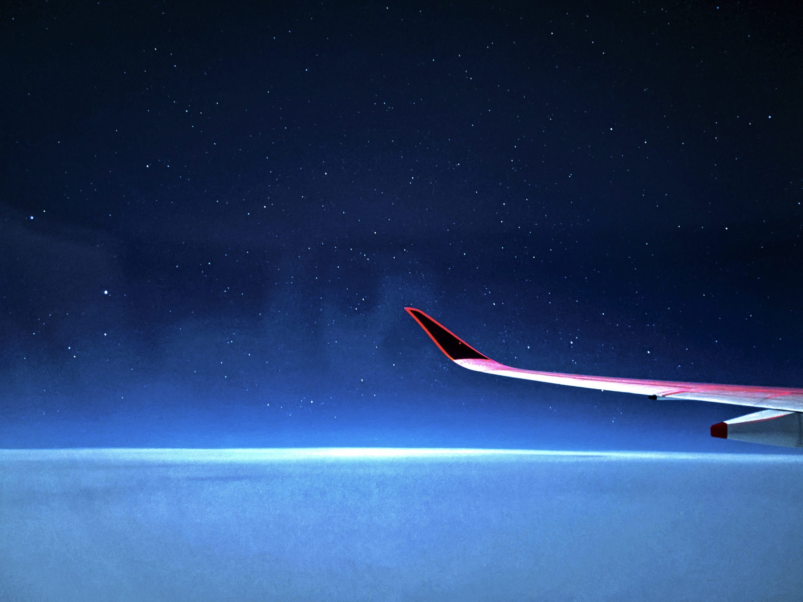 A serene view of an airplane wing at night, flying above the clouds with a starry sky in the background.