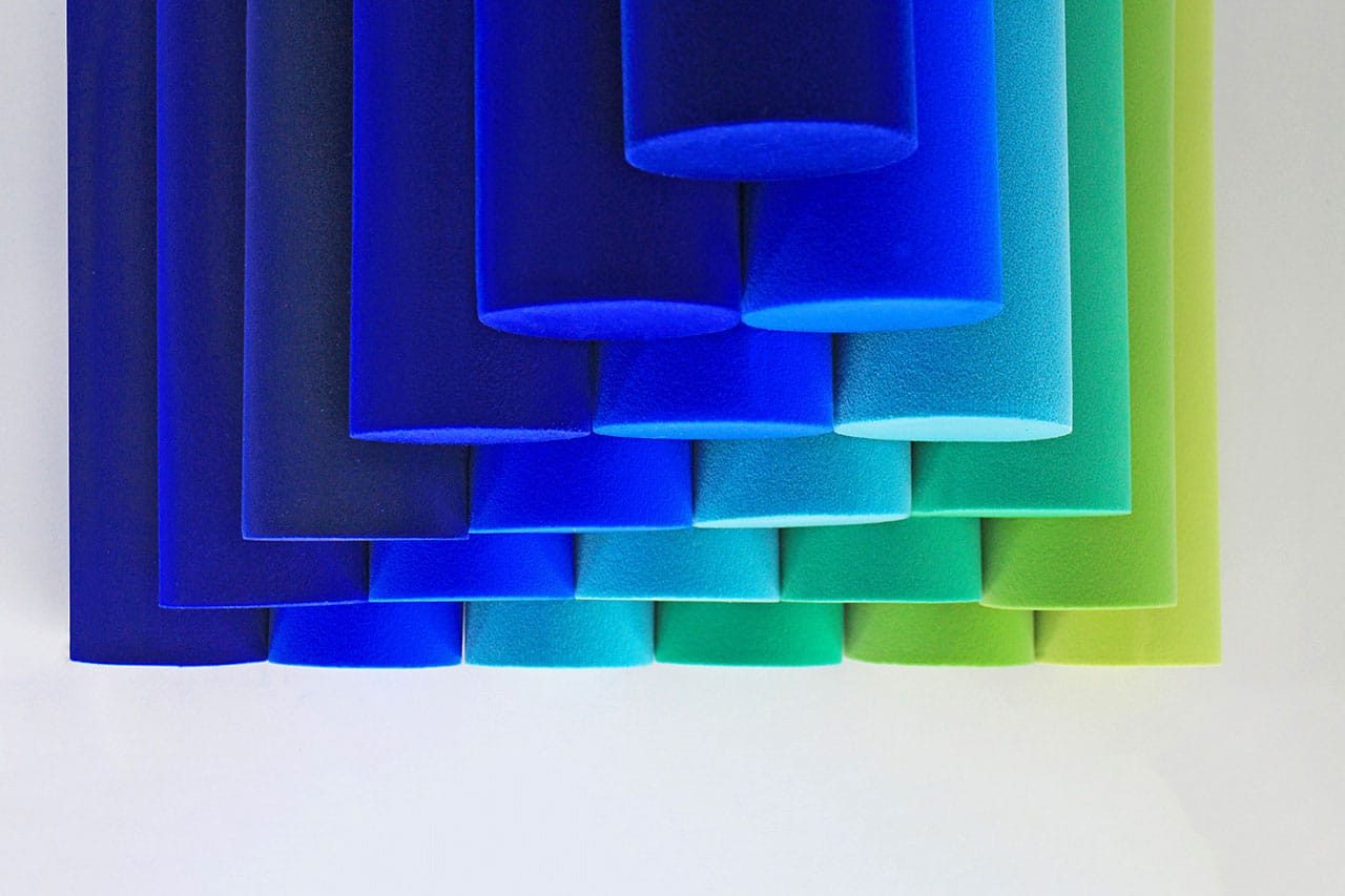 A series of cylindrical blue foam blocks in varying shades of blue and green, stacked in a gradient pattern against a white background.