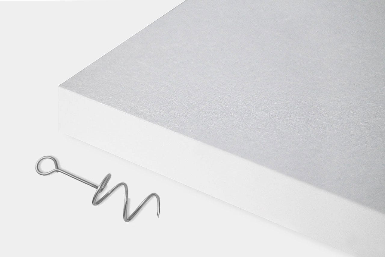 A single metal corkscrew lies on a white surface next to the corner of a thick, blank white book or notepad.