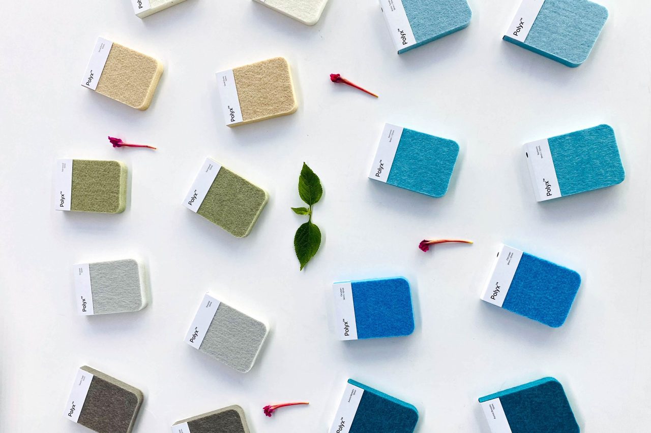 A neat arrangement of fabric sample squares in light colors such as white, beige, and shades of blue and green, laid out on a white background. Small leaves and pink flower petals are scattered between the samples.