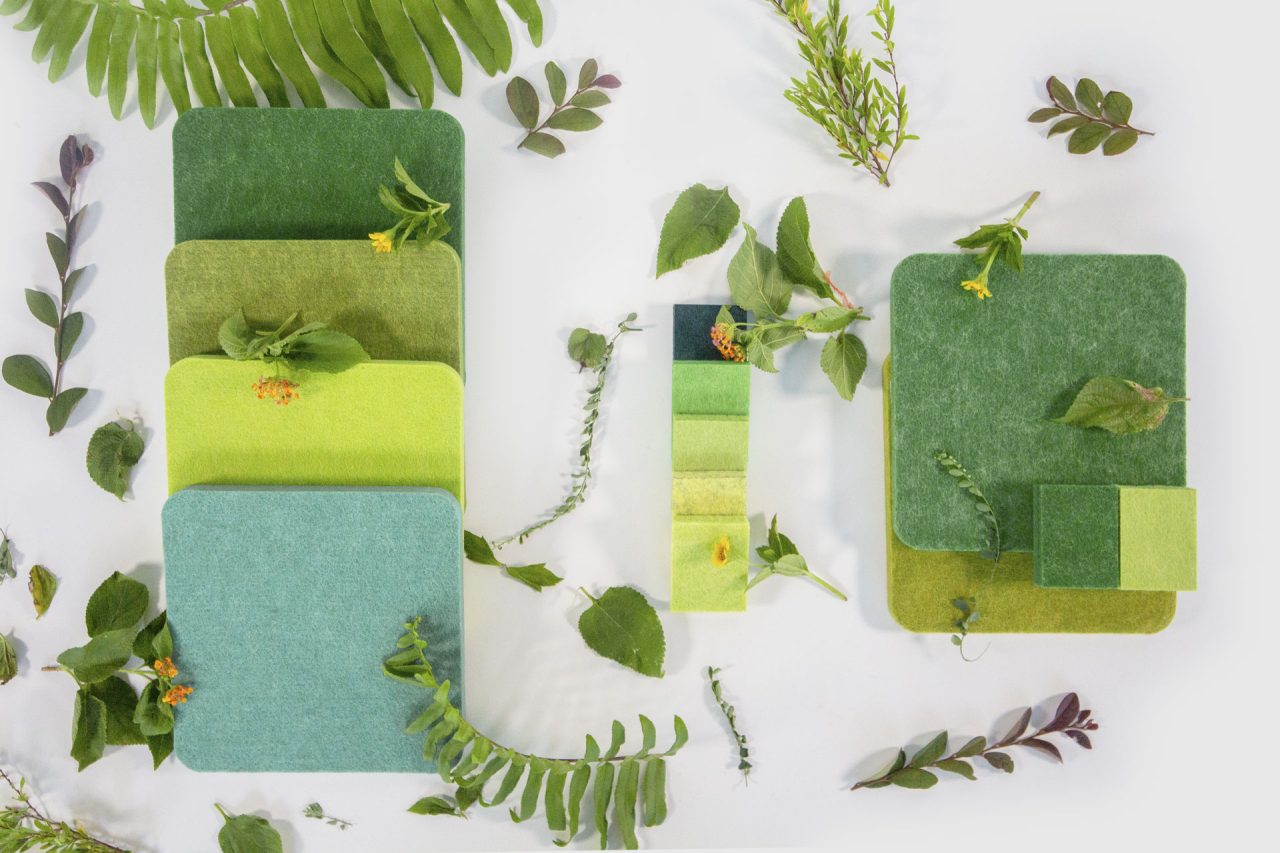 An array of green felt fabric samples arranged in various shades of green, with small leaves and plants placed around them, creating a nature-inspired aesthetic.